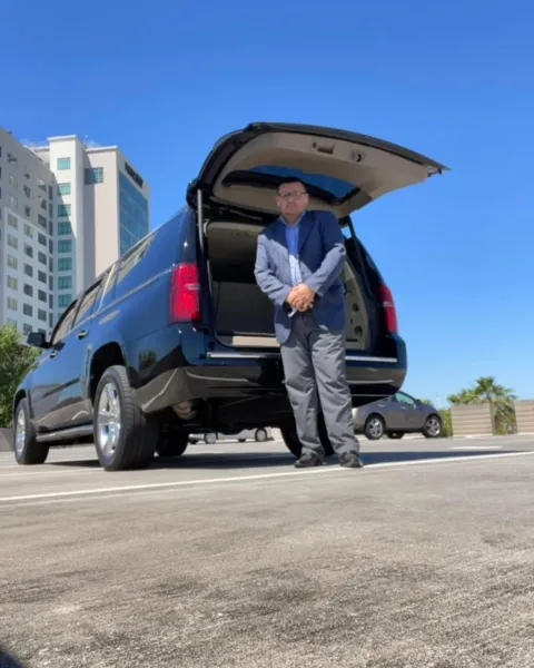 Chauffeur standing at the open liftgate of the black Suburban