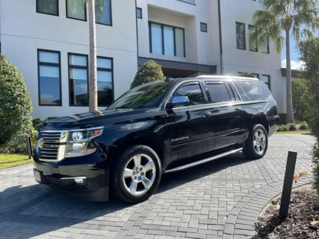 Black Chevrolet Suburban parked on a paver driveway lined with palm trees