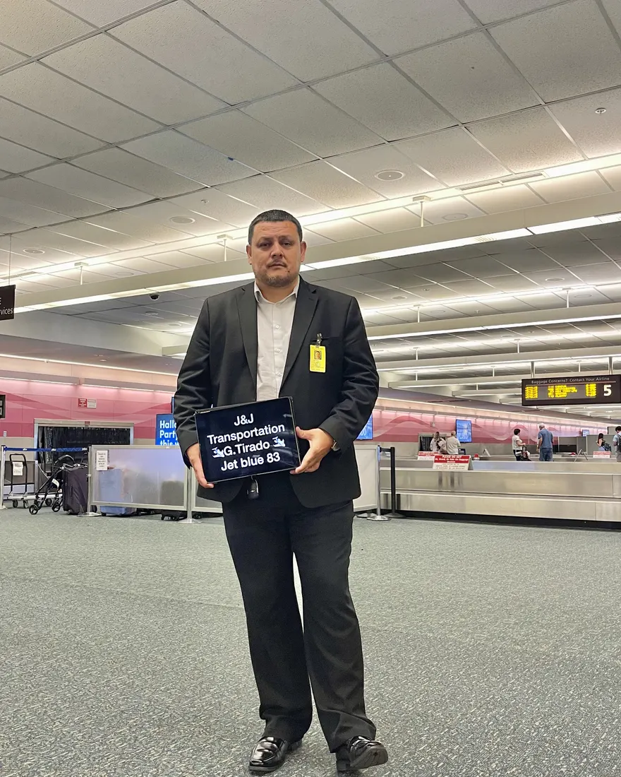 A suited J&J chauffeur holding a personalized welcome sign at baggage claim